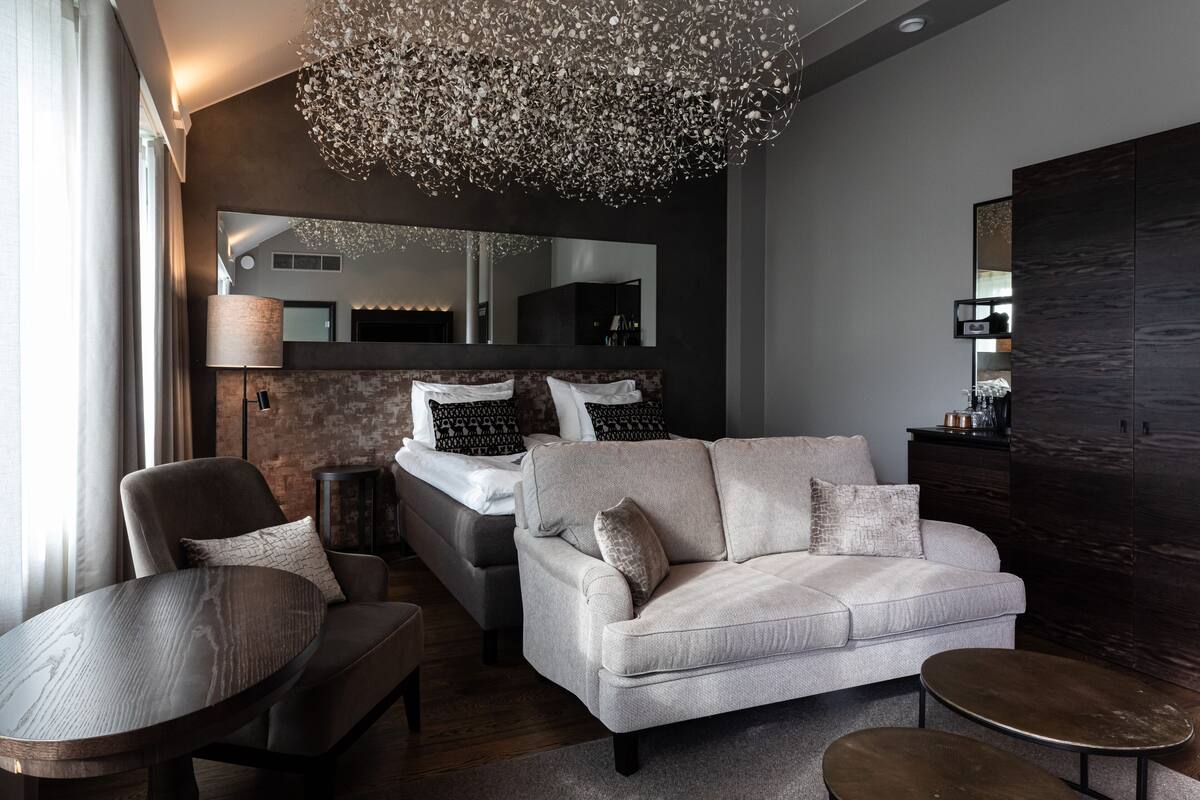 A modern bedroom with a large bed, a sofa, a chair, and a small table.