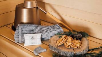 A sauna setting with a wooden bench, a massage table, a massage glove, a towel, a log with a carved design, and a sauna bag.