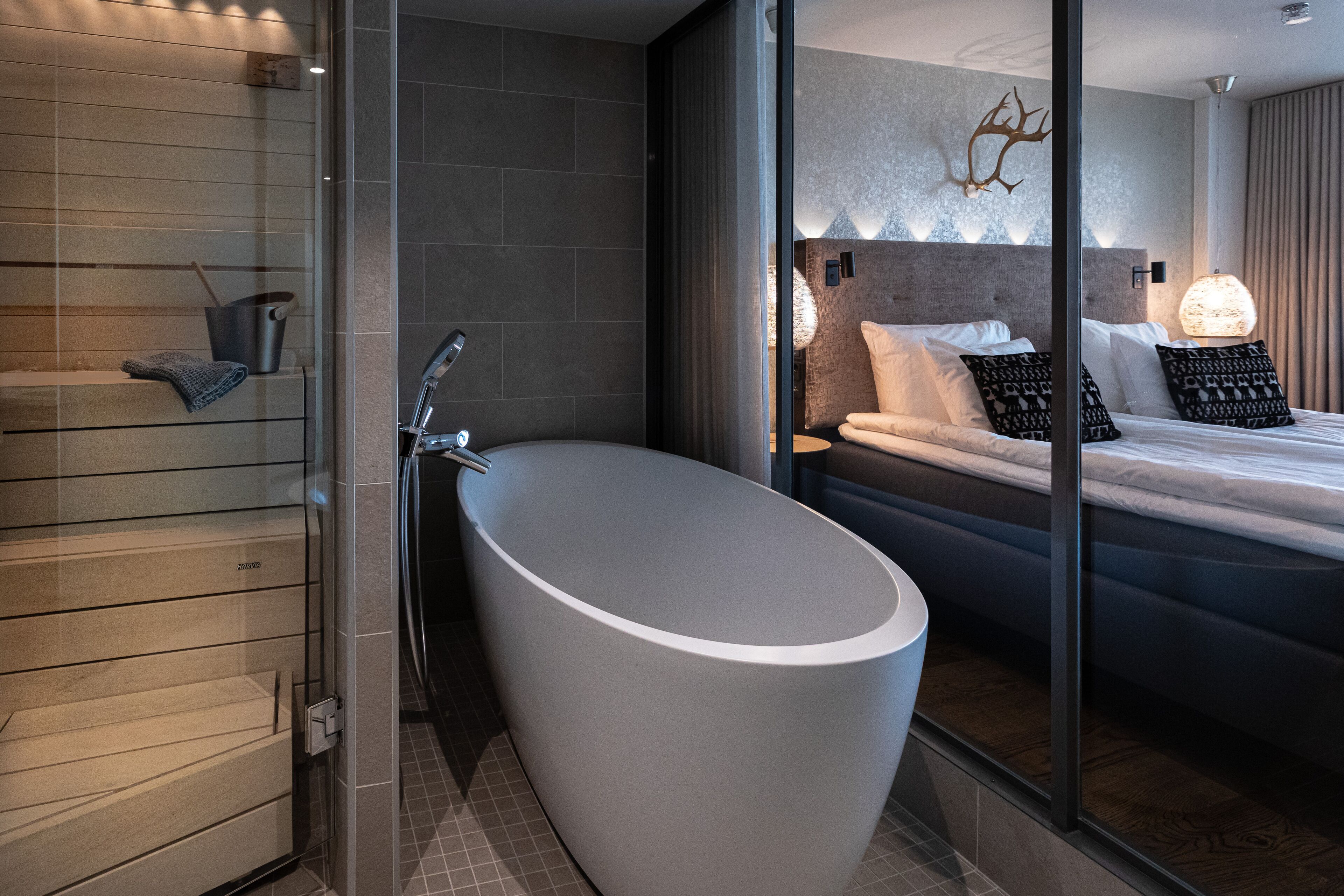Et moderne badeværelse med et fristående badekar, en brusekabine i glas og en seng med mønstrede puder.