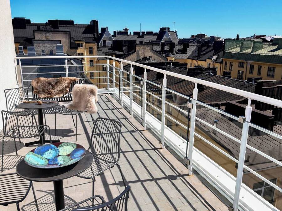 A balcony with metal chairs, a table, and a glass railing overlooking a cityscape.