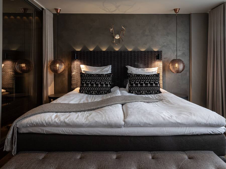 A modern bedroom with a large bed, a dark headboard, and two wall-mounted lamps.