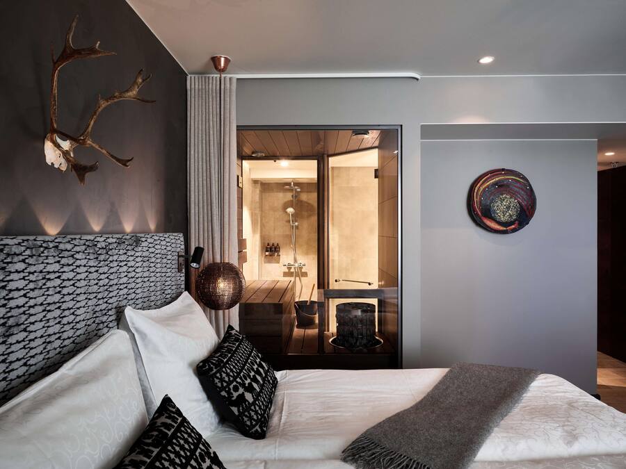 A modern bedroom with a large bed, a headboard with a unique pattern, a decorative wall piece, and a view into the bathroom.