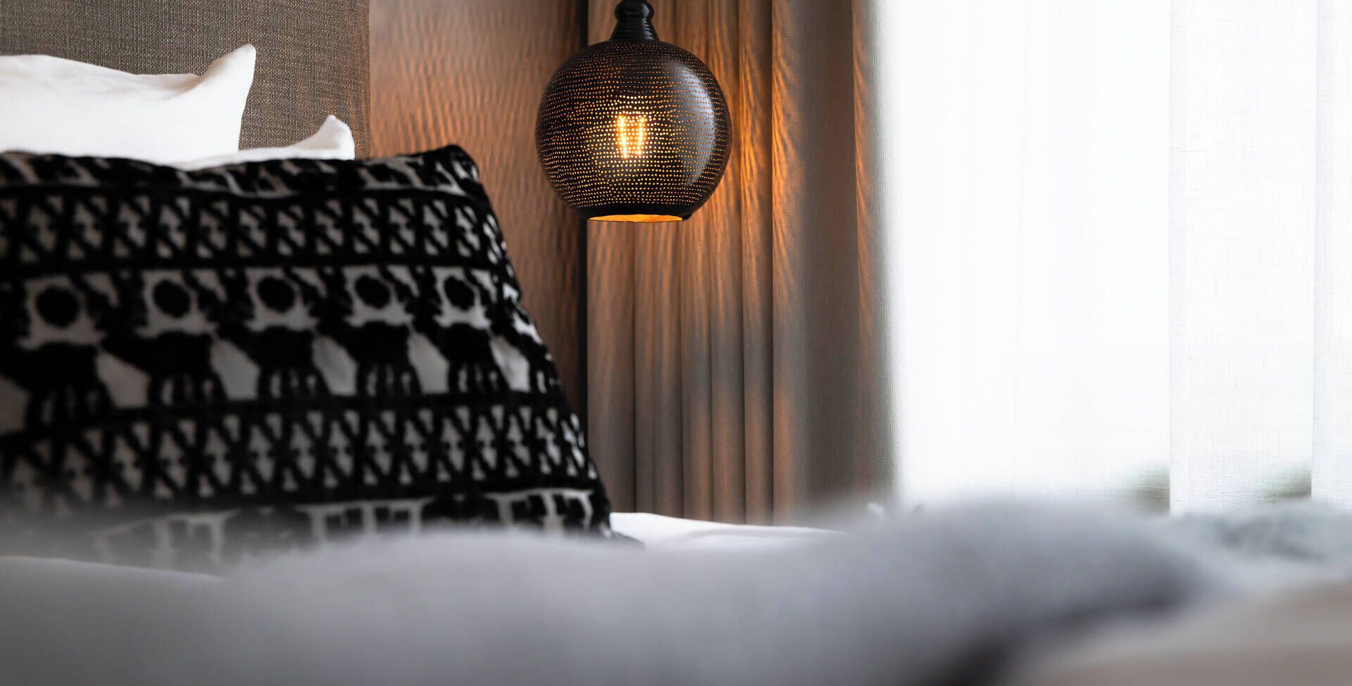 Una cama con almohadones estampados y una lámpara de pared con textura.