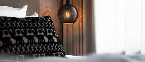 Una cama con almohadones estampados y una lámpara de pared con textura.