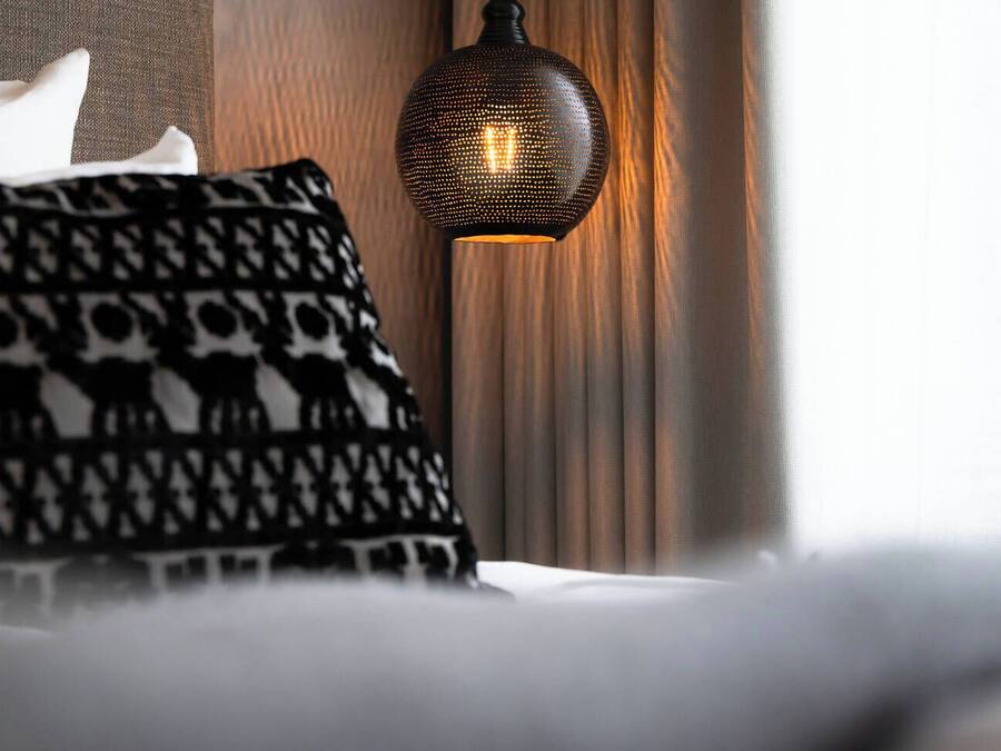 Una cama con almohadones estampados y una lámpara de pared con textura.