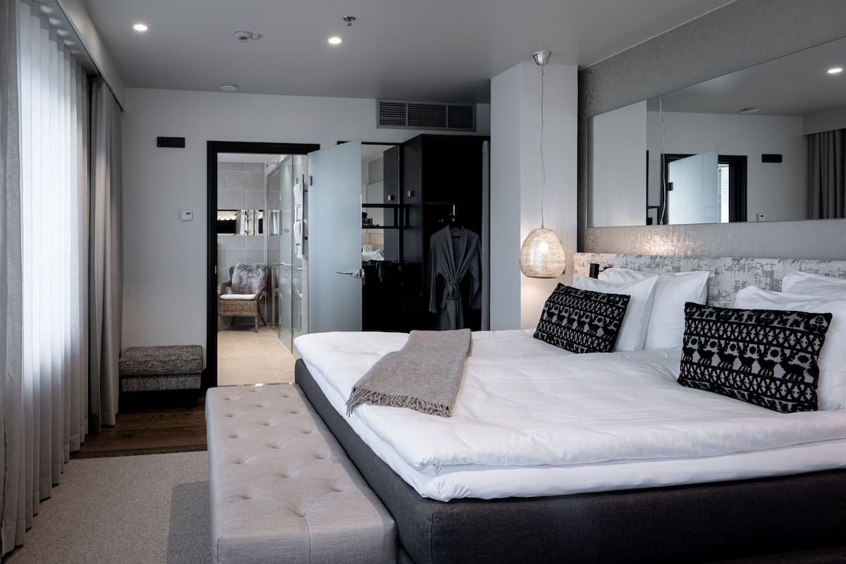A modern hotel room with a large bed, a seating area, and a walk-in closet.