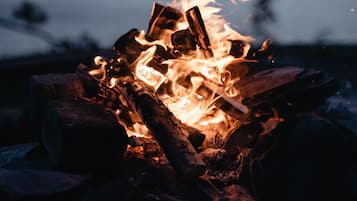 A campfire with logs and flames, set against a blurred background of a body of water and a dusky sky.