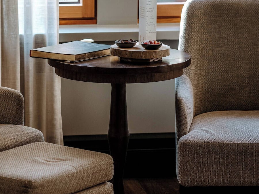 Una habitación con una mesa redonda de madera, dos sillones y un ventanal con cortinas.
