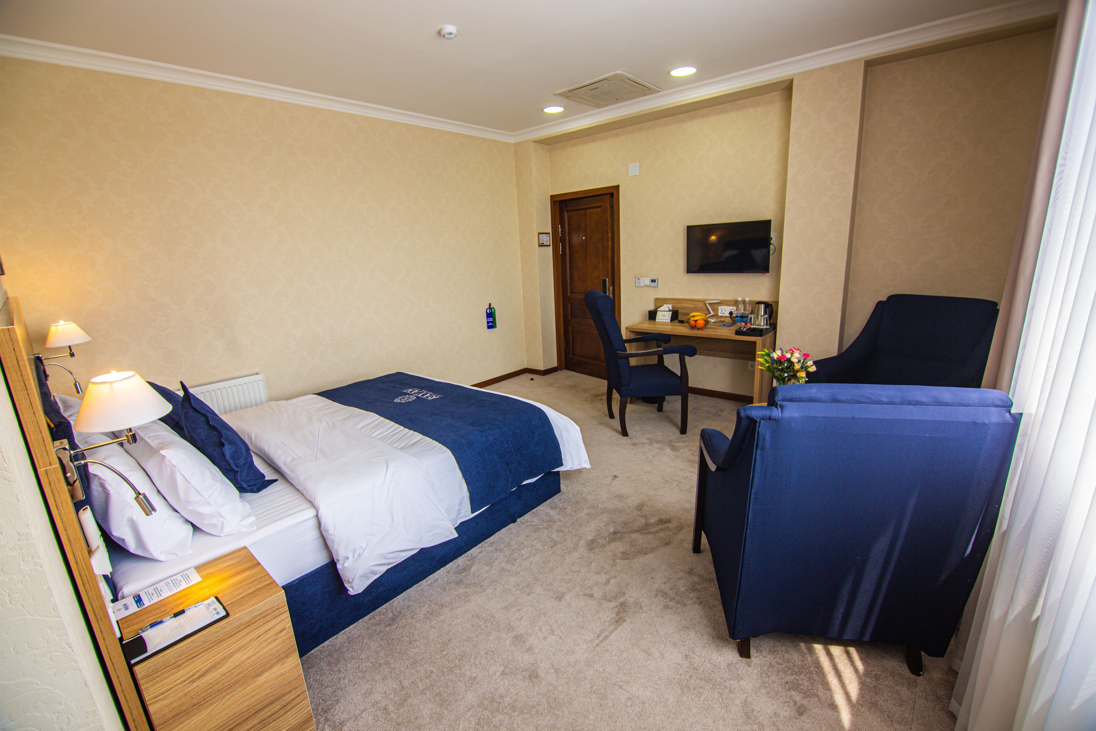 Ein Hotelzimmer mit einem Bett, einem Schreibtisch, einem Sessel und einem Fernseher an der Wand.