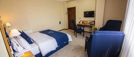 Ein Hotelzimmer mit einem Bett, einem Schreibtisch, einem Sessel und einem Fernseher an der Wand.