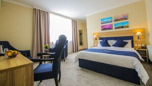 Quarto de hotel com cama, escrivaninha, cadeira e janela com cortinas.