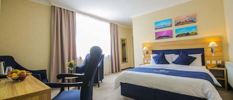 Una habitación de hotel con cama, escritorio, silla y ventana con cortinas.