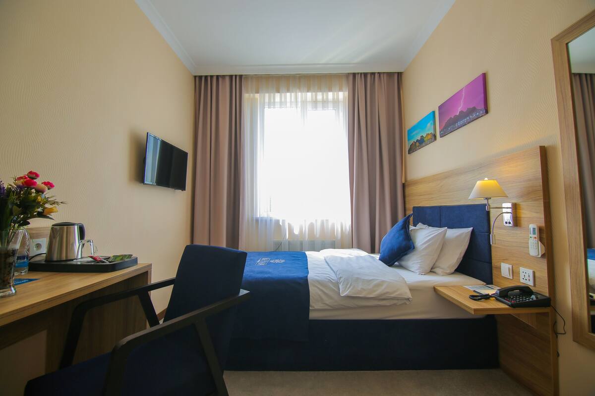 A hotel room with a bed, desk, chair, TV, and a window with curtains.