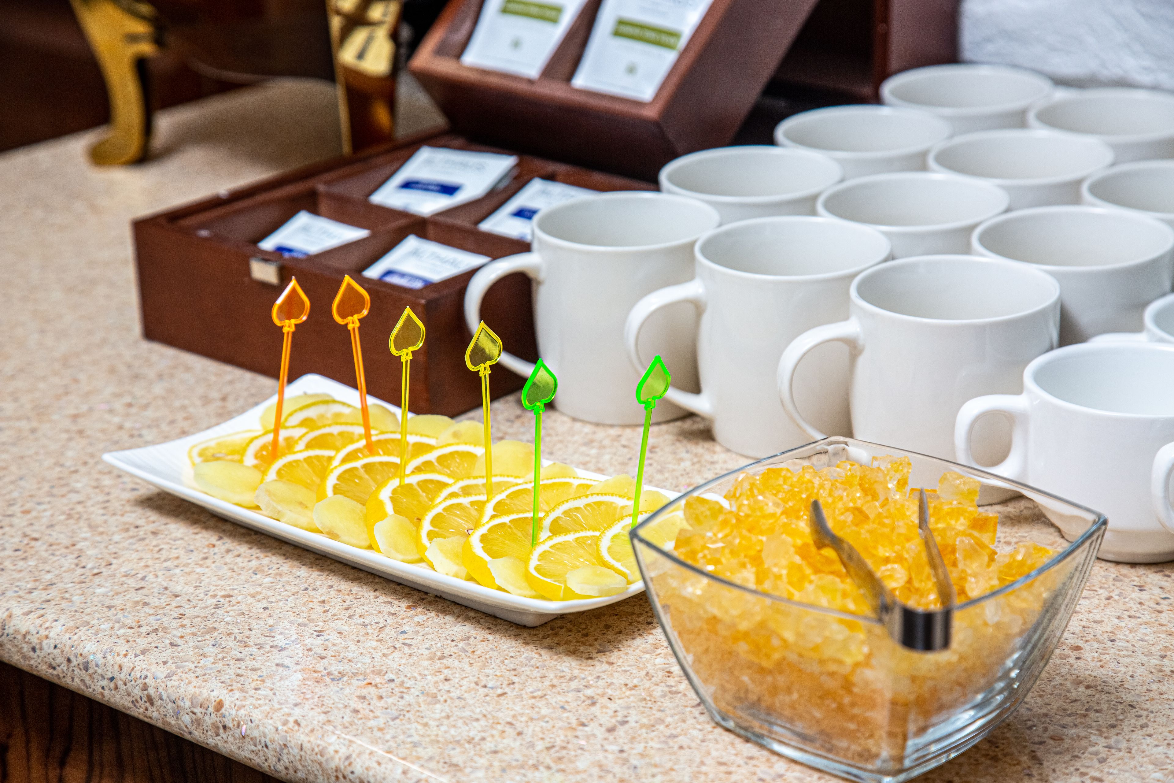 A buffet setup with a plate of sliced oranges and a bowl of sugar cubes.