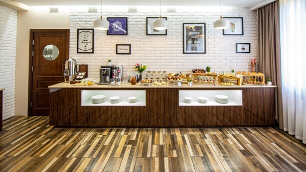 Um balcão de pequeno-almoço com diversas opções de comida, uma máquina de café e uma parede decorada com fotografias emolduradas e um relógio.