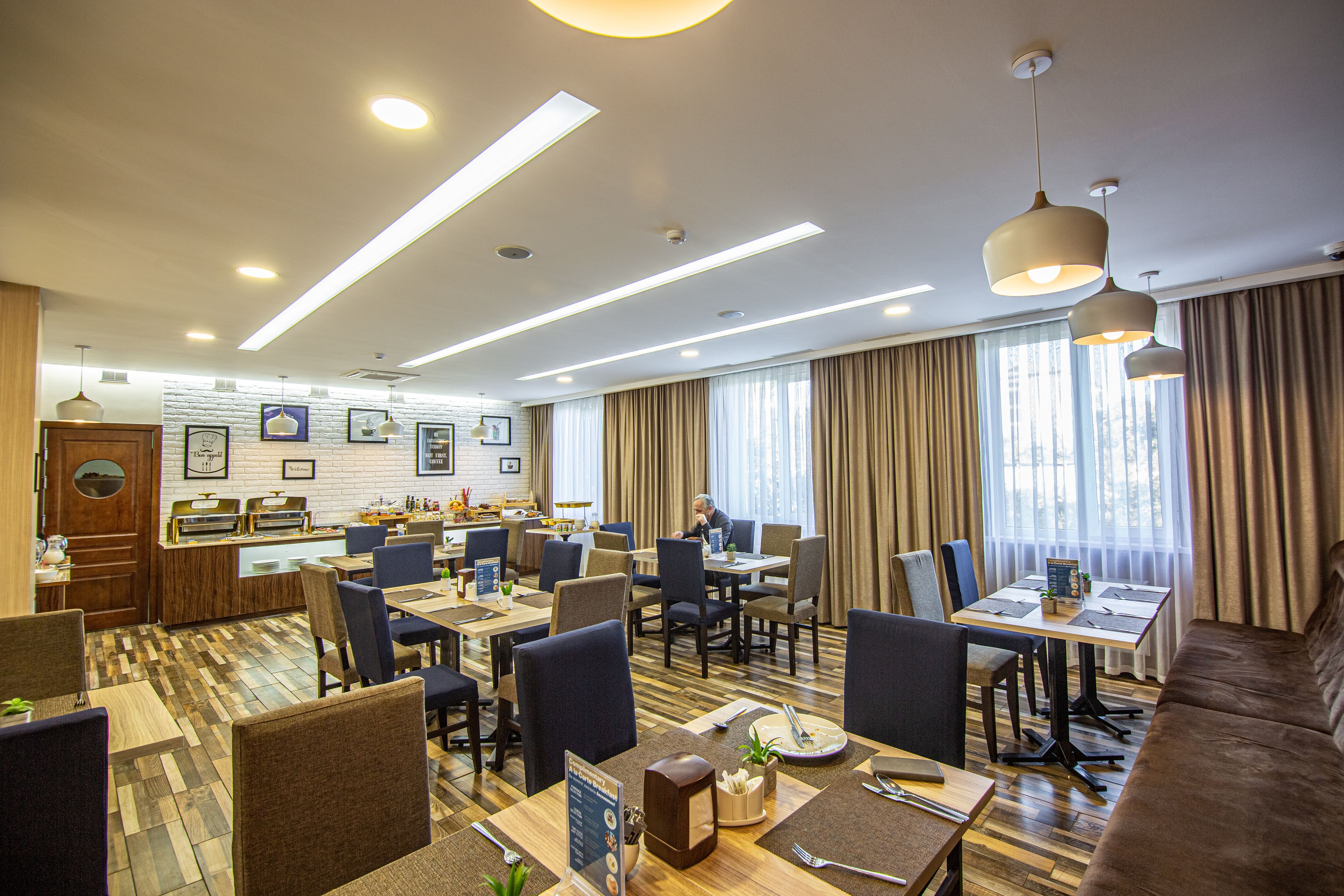 Une salle à manger d’hôtel avec plusieurs tables et chaises, un comptoir de réception et une cuisine en arrière-plan.