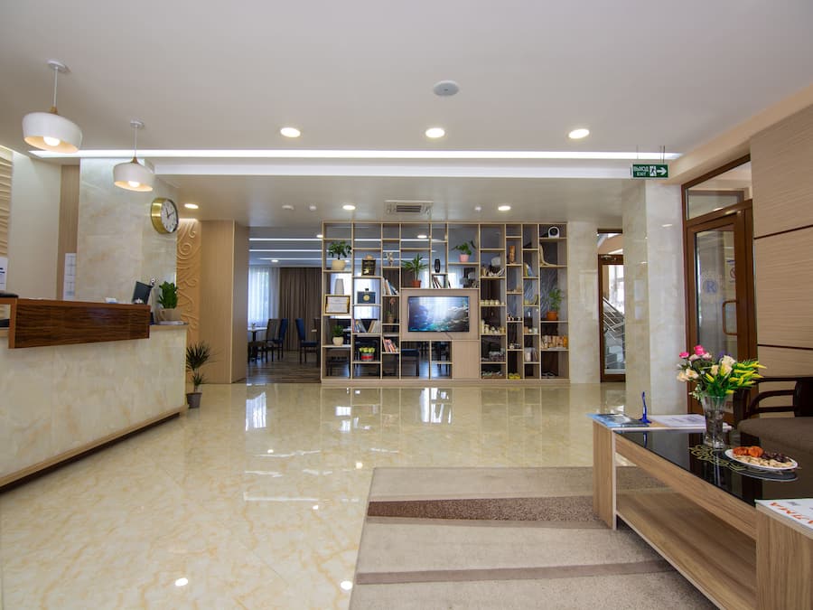 A hotel reception area with a marble floor, a reception desk, a TV, and a seating area with a vase of flowers.