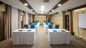 Uma sala de conferência com mesas, cadeiras dispostas em fileiras e um quadro branco na parede do fundo.