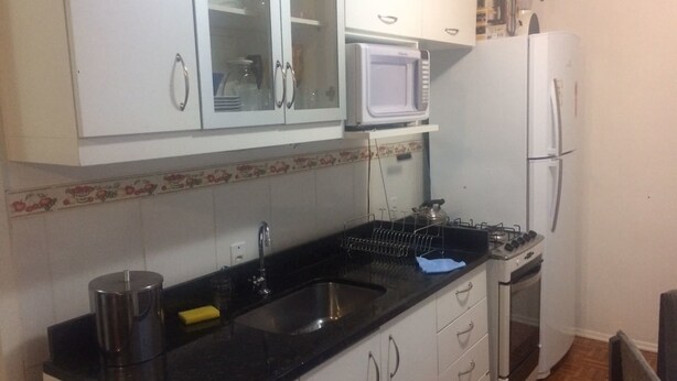 Eine Küche mit weißen Schränken, einer schwarzen Arbeitsplatte, einer Mikrowelle, einem Kühlschrank und einem Backofen.