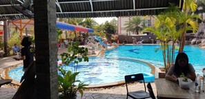 Une piscine avec un toboggan, entourée de palmiers et dotée d’un espace détente abrité.