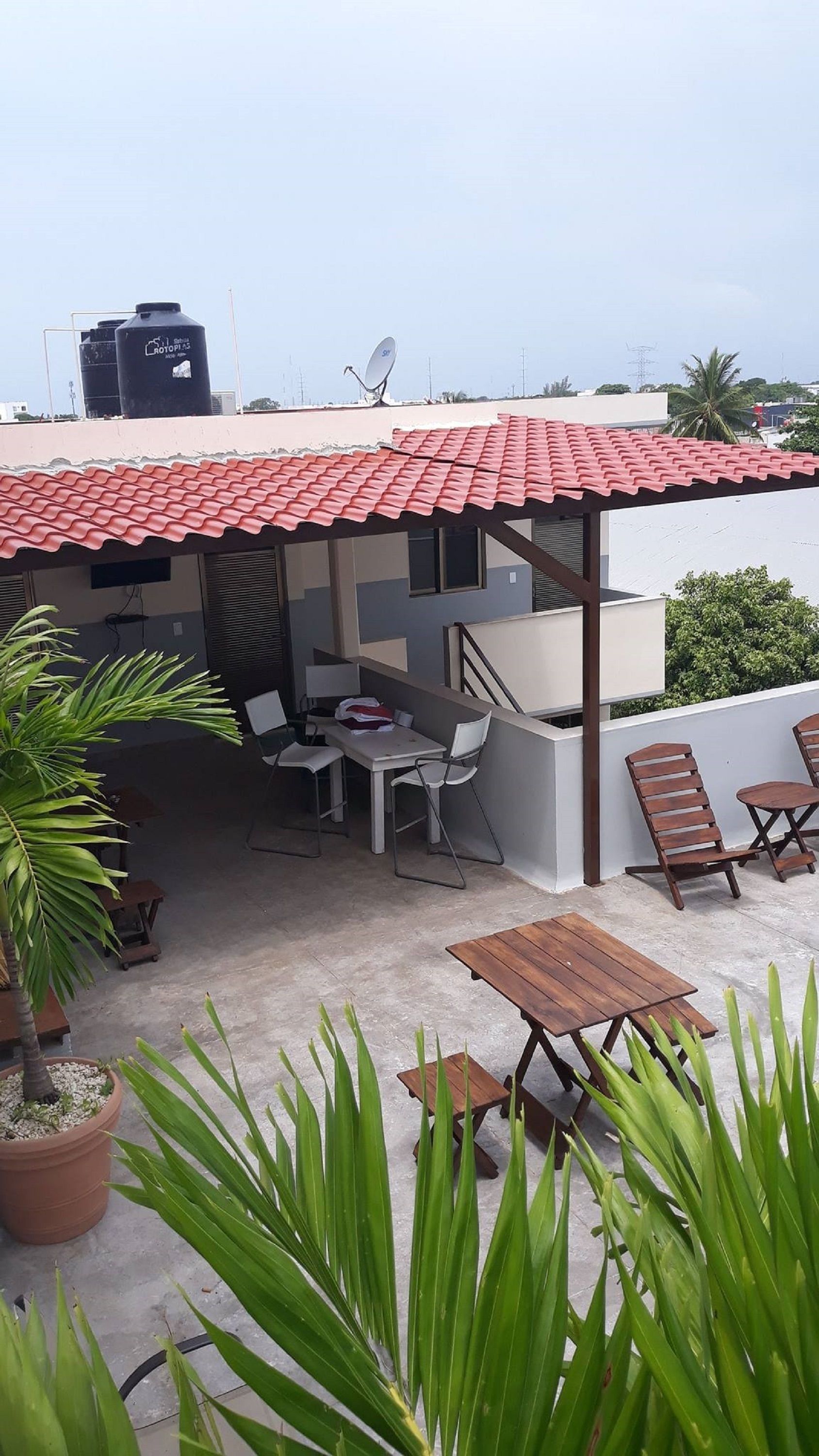 An outdoor patio with a red-tiled roof, a table, chairs, and potted plants.