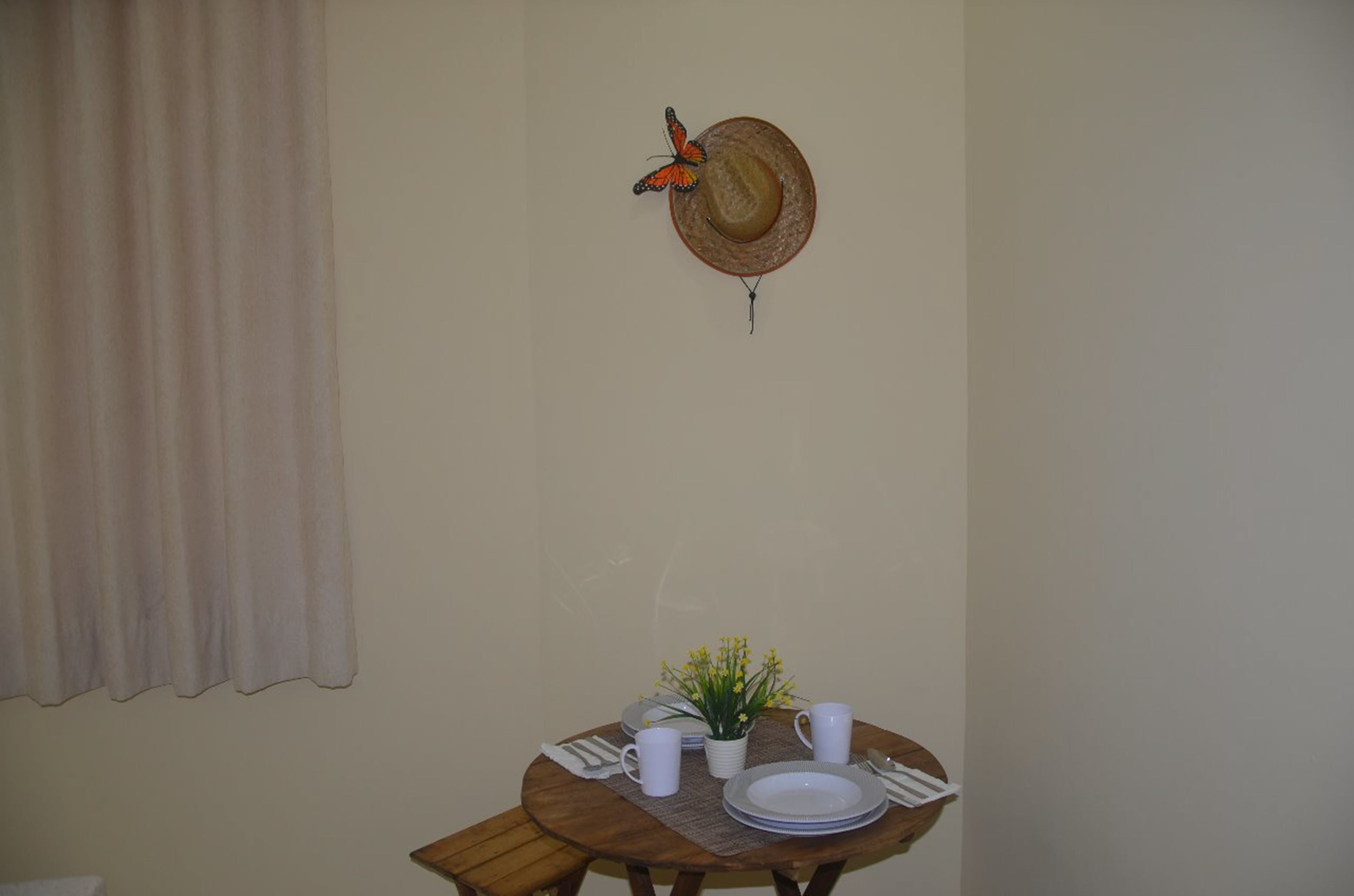 Uma mesa de jantar com um chapéu e decoração de borboleta, uma pequena planta, e pratos e xícaras brancas.