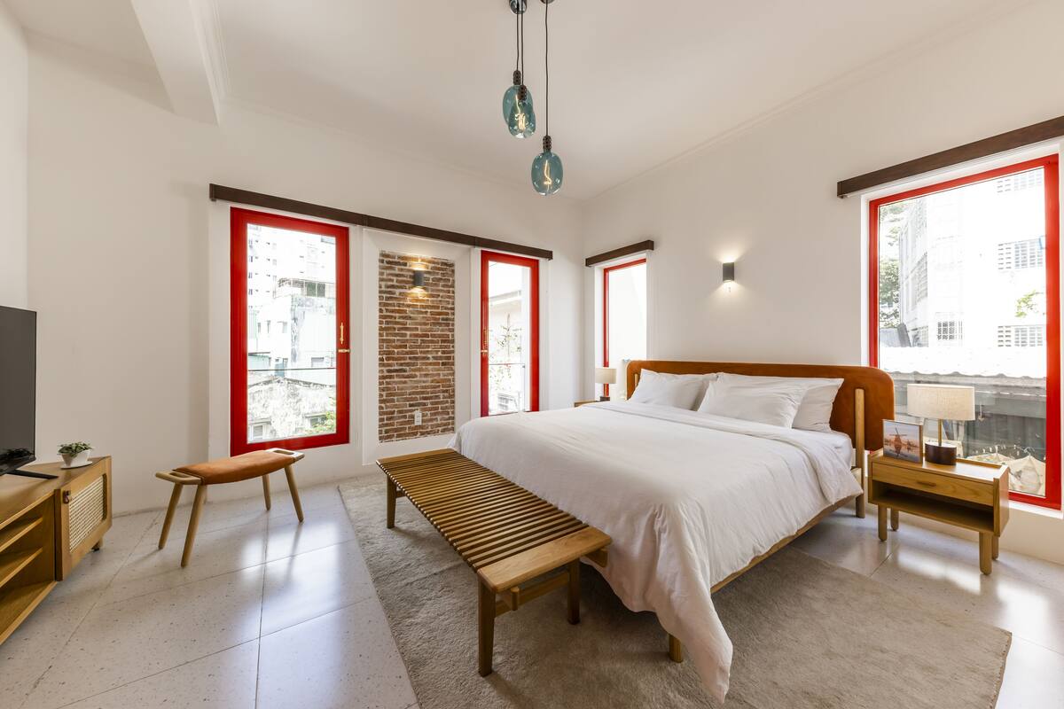 Un dormitorio moderno con una cama grande, una banca de madera y un ventanal con marco rojo.
