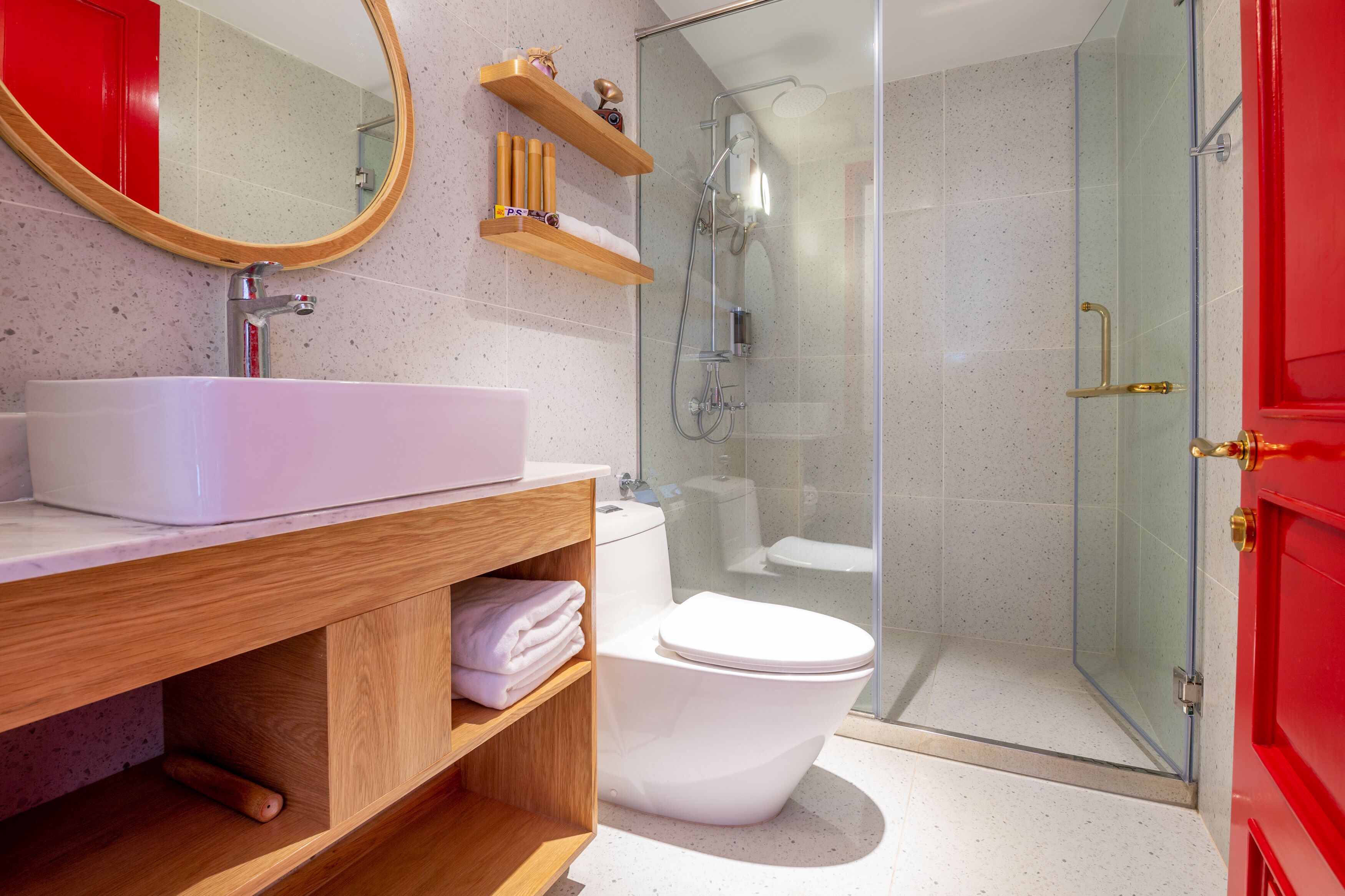 Un baño moderno con lavamanos blanco, tocador de madera, cabina de ducha de vidrio y un armario rojo.