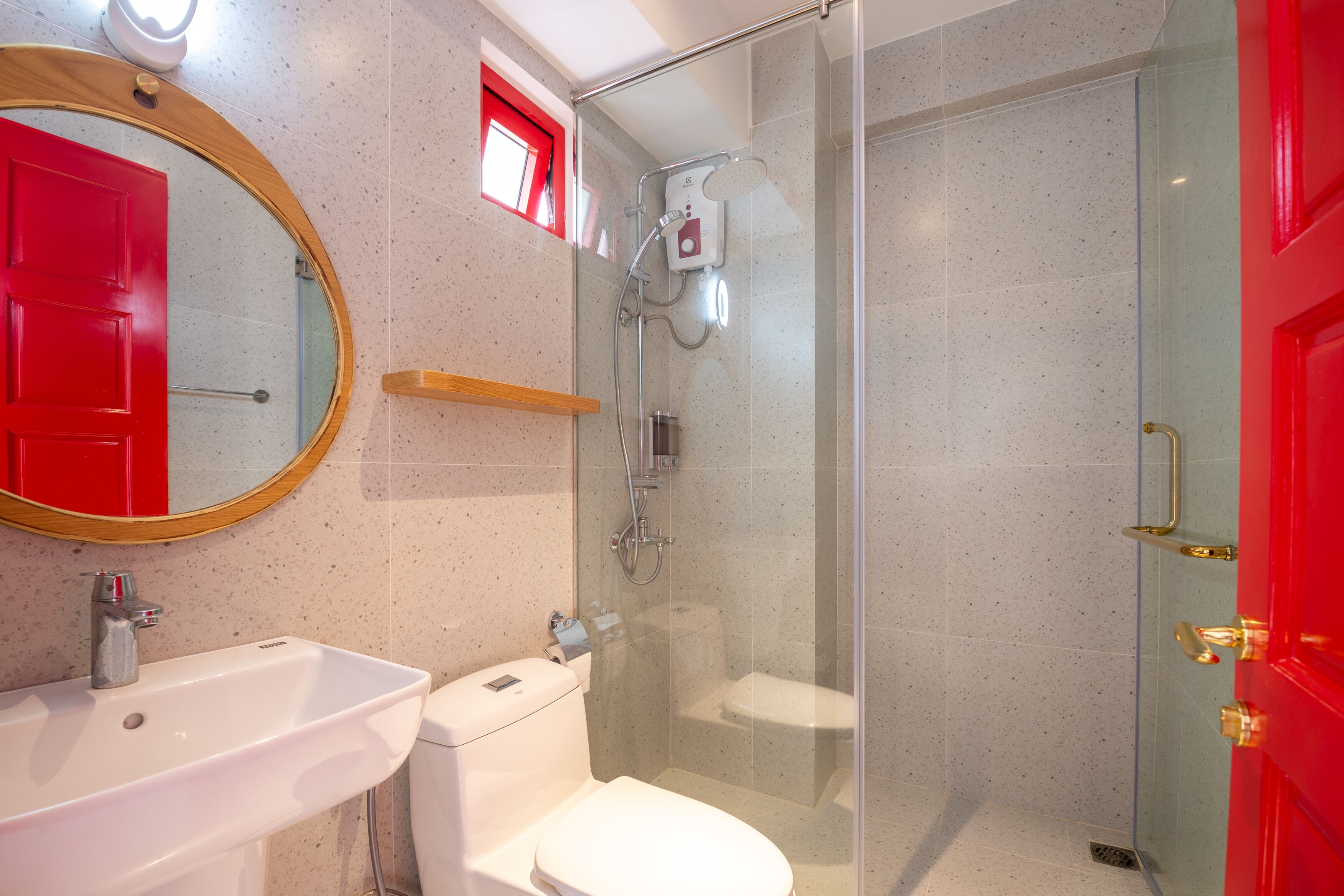 Un baño con cabina de ducha de vidrio, un lavamanos blanco y una puerta roja.