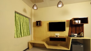 A compact room with a built-in TV, a small refrigerator, and a wooden bench. - Hotel Elite Continental - Airport Road Andheri (Mumbai)