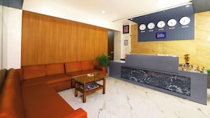 A modern reception area with a wooden panel wall, a reception desk with clocks displaying time zones, and a marble inlay. - Hotel Elite Continental - Airport Road Andheri (Mumbai)