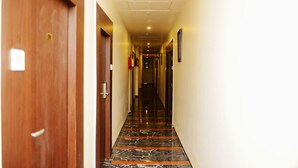 A hallway with a wooden door on the left, a fire extinguisher on the wall, and a framed picture on the right. - Hotel Elite Continental - Airport Road Andheri (Mumbai)