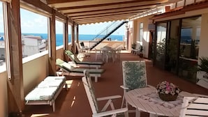 A covered outdoor area with lounge chairs, a table with a floral centerpiece, and a staircase leading to an upper level. - I Faraglioni (Terrasini)