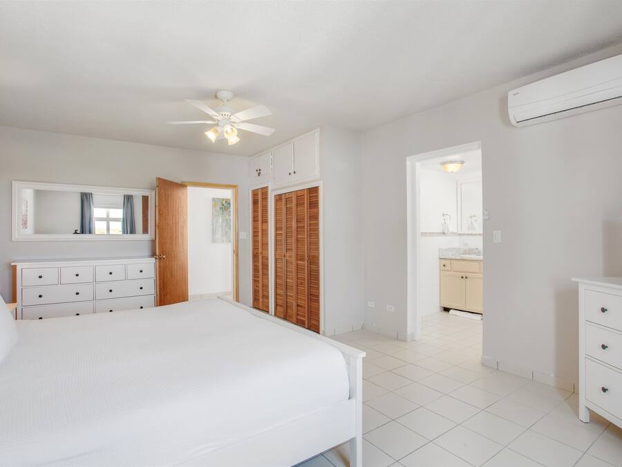 A bedroom with a bed, a dresser, a TV, and a ceiling fan.