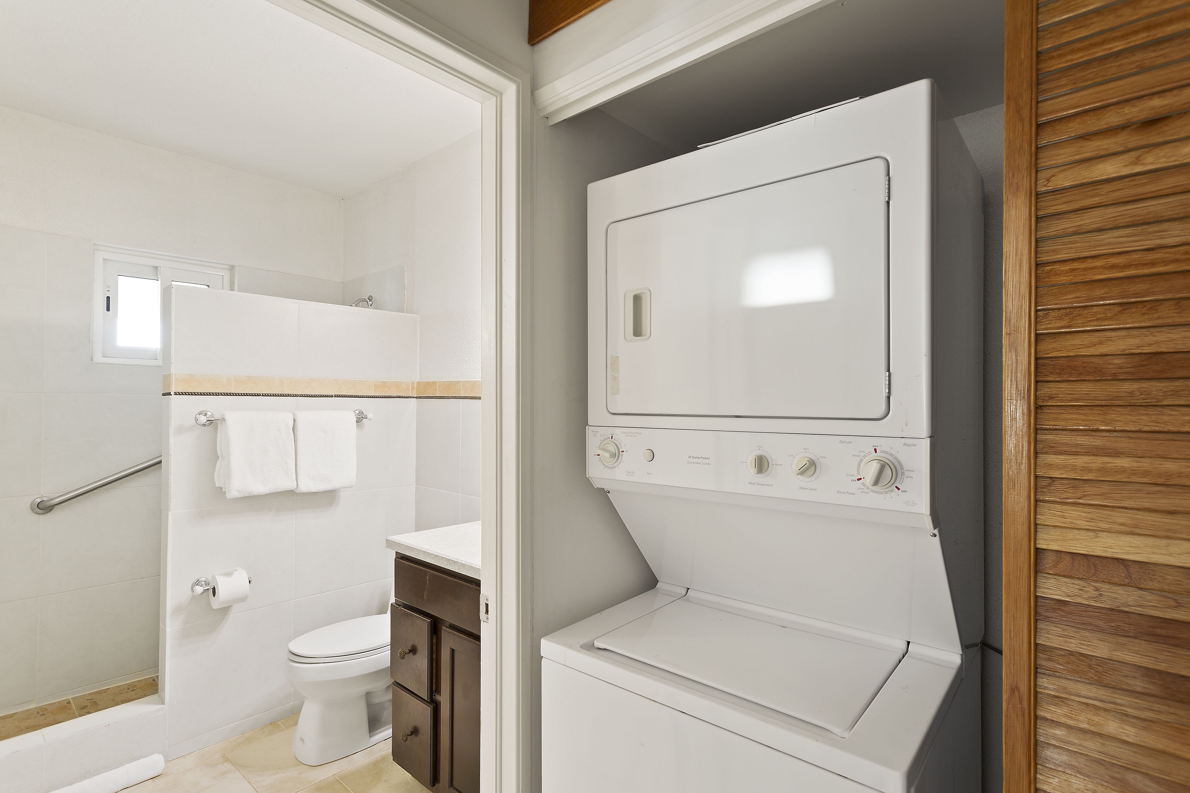 A compact, modern bathroom with a built-in washer and dryer, a toilet, and a shower area.