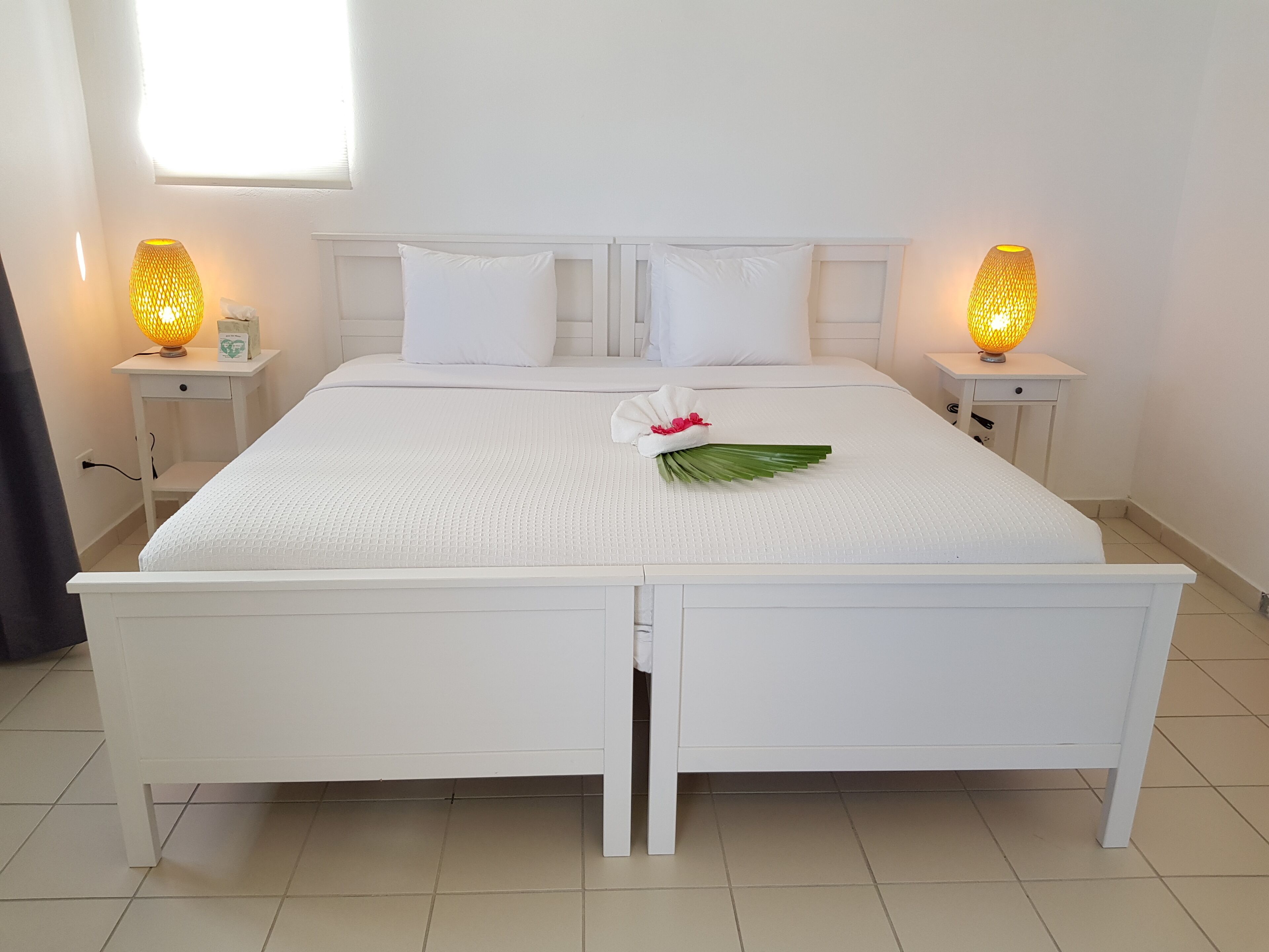 A neatly made bed with white bedding and pillows, two bedside lamps, and a decorative leaf on the bed.