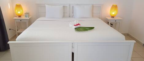 Una cama bien hecha con ropa de cama y almohadas blancas, dos lámparas de noche y una hoja decorativa sobre la cama.