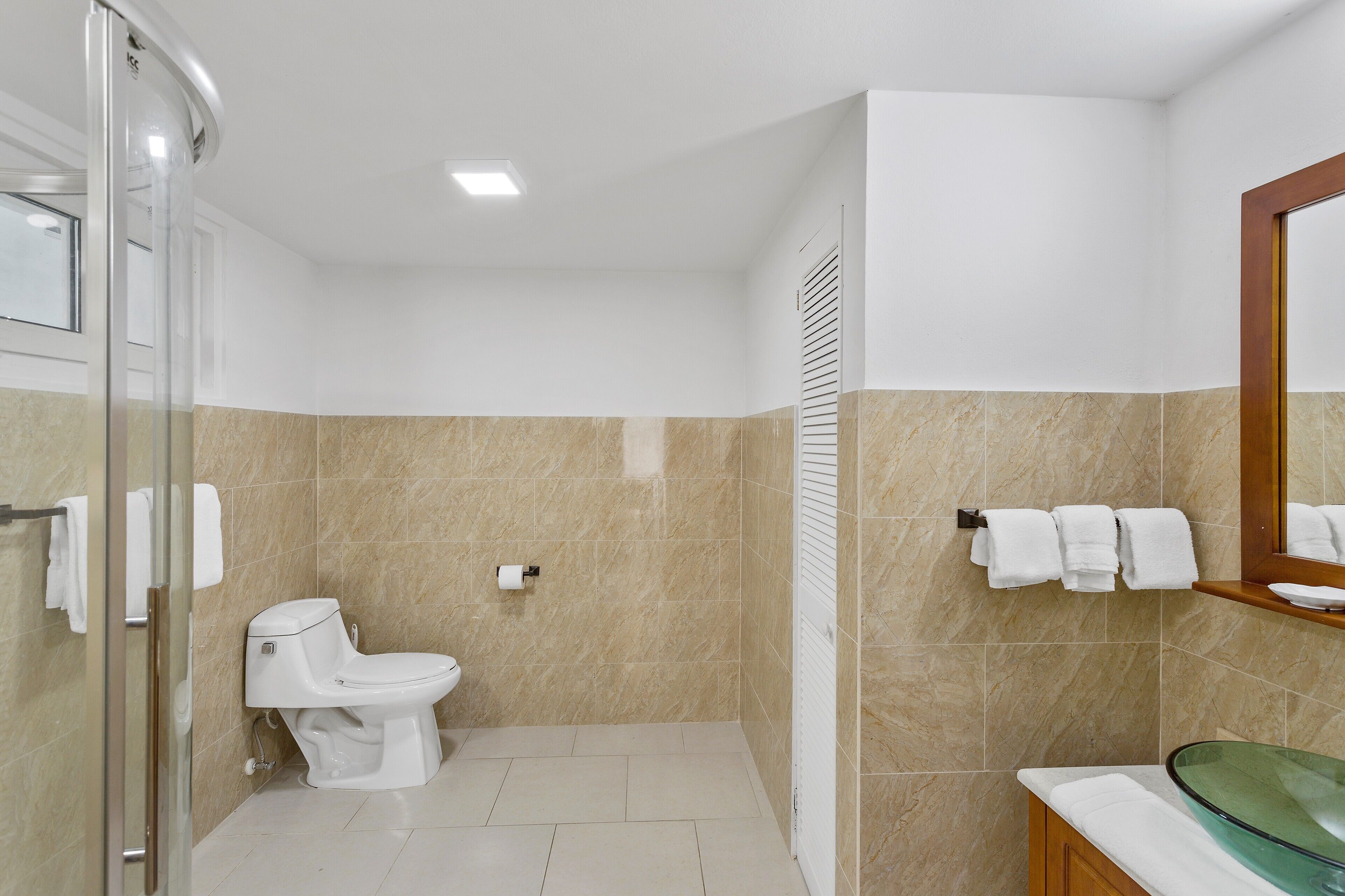 A bathroom with a toilet, a glass shower enclosure, a sink with a glass basin, and a towel rack with towels.