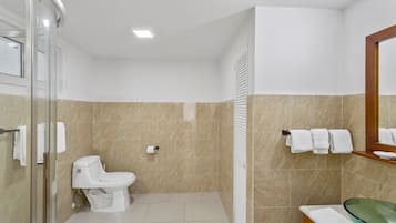 A bathroom with a toilet, a glass shower enclosure, a sink with a glass basin, and a towel rack with towels.