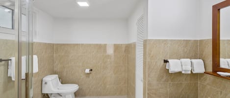 A bathroom with a toilet, a glass shower enclosure, a sink with a glass basin, and a towel rack with towels.