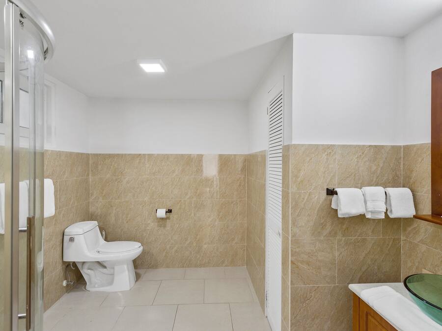 A bathroom with a toilet, a glass shower enclosure, a sink with a glass basin, and a towel rack with towels.