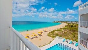 A beach view from a balcony with a pool, sun loungers, and umbrellas. - Turtles Nest Beach Resort  (West End Village)