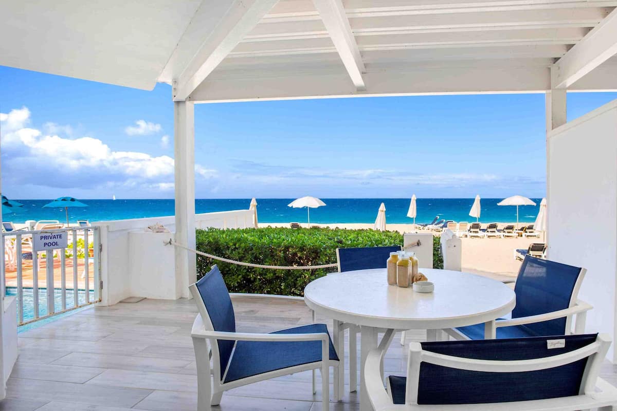 Un espace piscine privé avec une table et des chaises, donnant sur une plage agrémentée de parasols et de chaises longues.