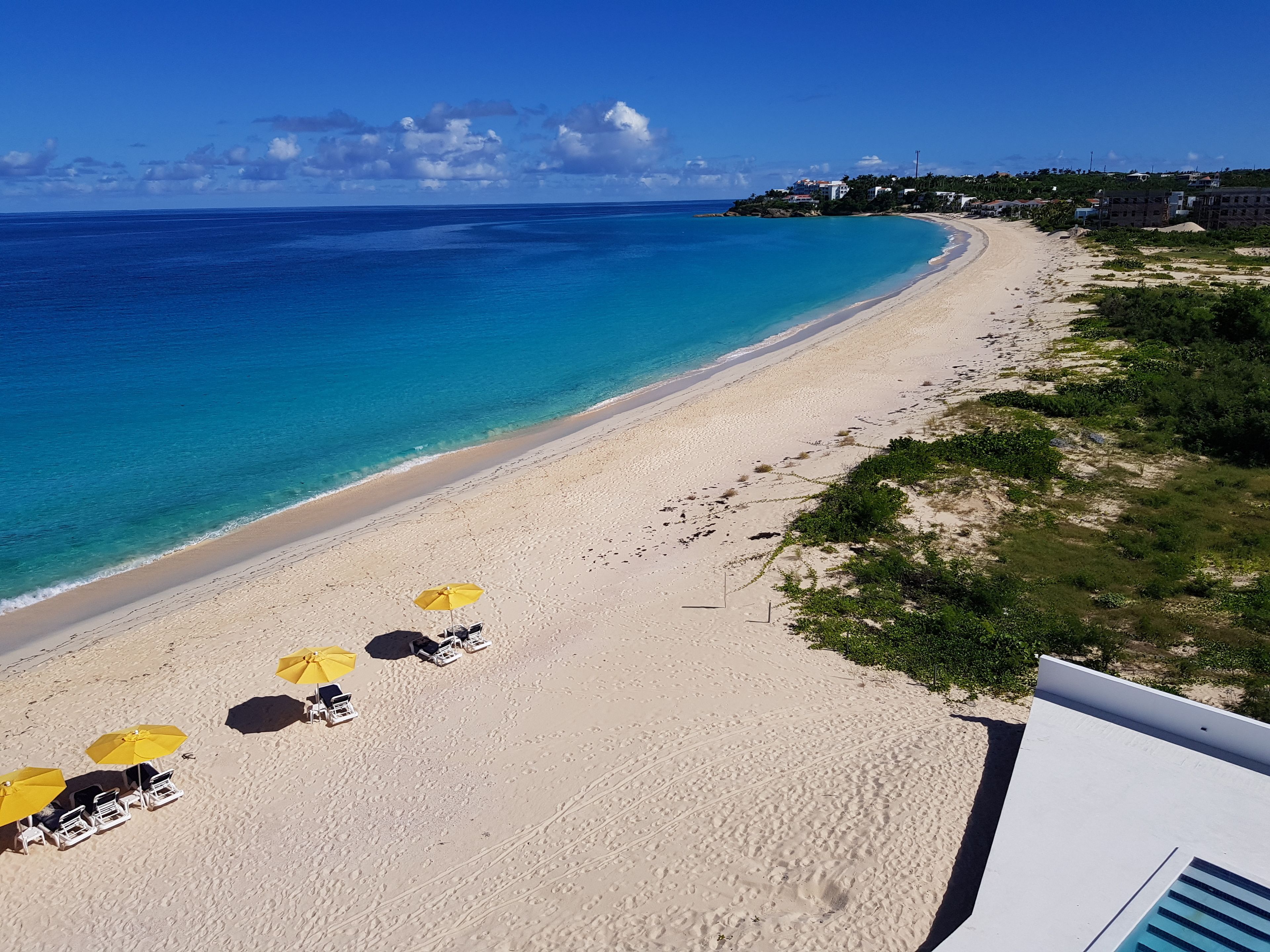 A beach with clear blue water, a sandy shore, and several yellow umbrellas.