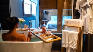 A woman in a bathtub with a tray of amenities, a window with a view of the outside, and towels hanging on a rack. - Wood Hotel Gramado (Gramado)