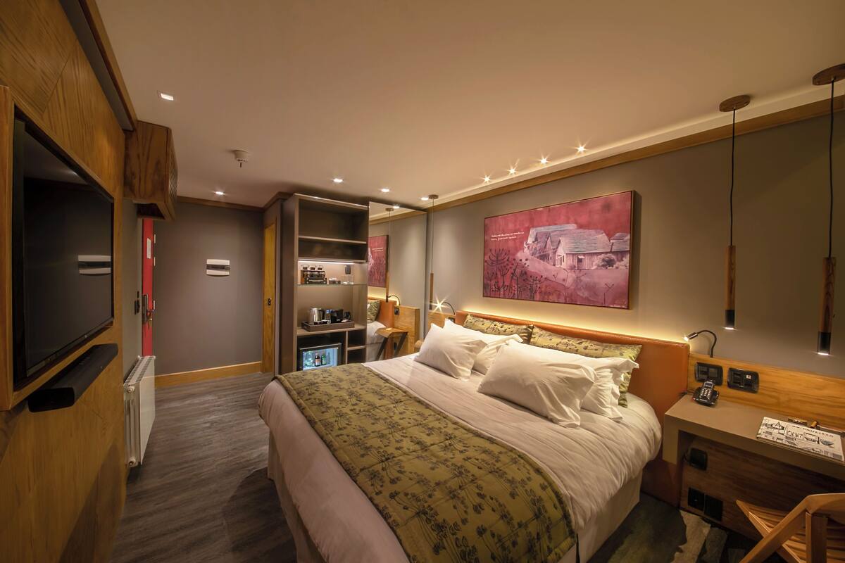 A hotel room with a bed, a TV, a desk, and a mirror.