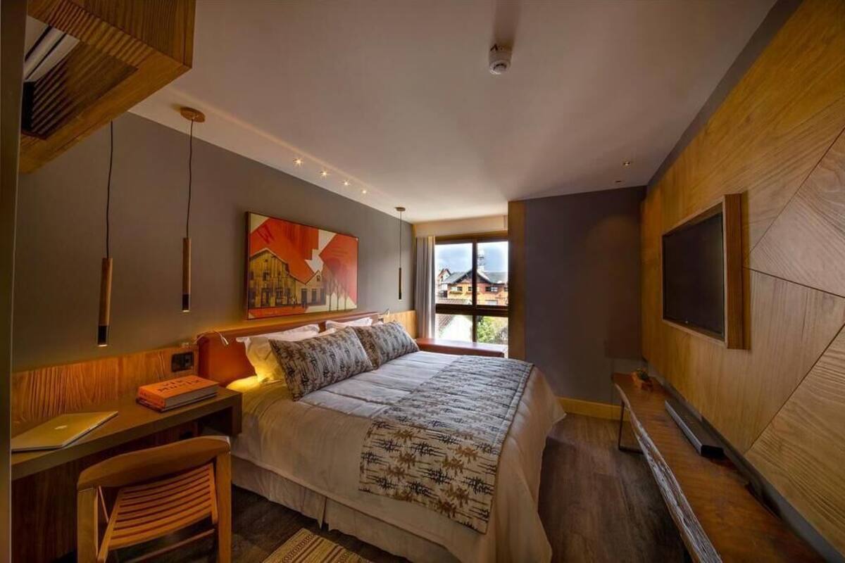 A modern bedroom with a large bed, a desk, and a TV mounted on the wall.
