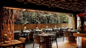 An indoor dining area with wooden tables and chairs, a vertical garden wall, and a wooden ceiling with geometric patterns. - Wood Hotel Gramado (Gramado)
