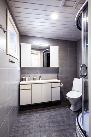 Casa de banho moderna com teto de madeira, azulejos cinzentos, toucador branco com espelho, sanita e cabine de duche em vidro.