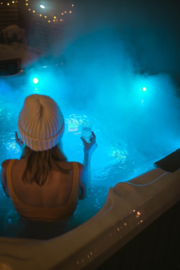 A person in a hot tub with blue lighting, holding a glass.